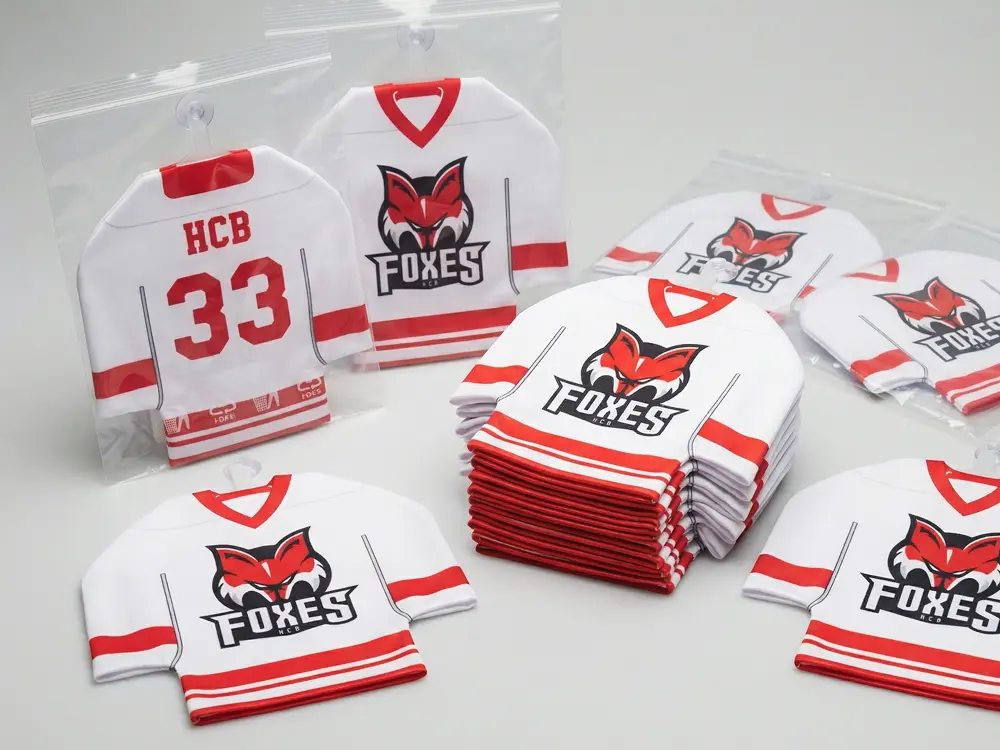 Mini-Eishockeytrikots mit breitem Schnitt und individuellem Aufdruck im Vereins-Design, inklusive Mini-Kleiderbügel für die Befestigung an Scheiben.